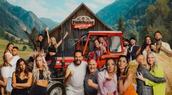 Auf dem Gruppenbild zur Show Forsthaus Rampensau Germany stehen vor einer alpinen Holzhütte zahlreiche Kandidat*innen, darunter Melina Hoch mit Max Bornmann, Eva Benetatou, Walentina Doronina, Leon.Content, Gina Beckmann, Maurice Dziwak mit Vater Frank, Yeliz Koc, Dilara Kruse, Paul Aubster, Oliver Gaukel, Christo, C-Bas, Marc Robin Wenz, Henna, Bernhard Schwendemann und Sarah Knappik. Die Stimmung ist ausgelassen und voller Vorfreude.