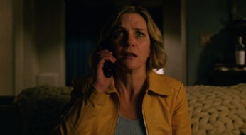 Auf dem Bild aus der Serie Pluribus ist Rhea Seehorn in ihrer Rolle zu sehen. Sie trägt eine gelbe Jacke und hält ein Telefon ans Ohr, während sie mit besorgtem Blick in die Ferne schaut. Die Beleuchtung ist düster.
