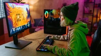 Beim Cloud-Gaming Vergleich zeigt dieses Bild eine junge Person mit grüner Mütze und Kapuzenpullover, die an einem RGB-beleuchteten Gaming-Setup spielt, während ein farbenfrohes Spiel auf dem Monitor läuft.