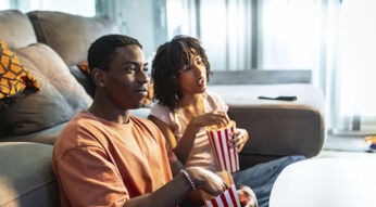 Ein junges Paar sitzt vor dem Sofa auf dem Boden und schaut Fernsehen.