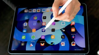 Weibliche Hand mit Apple Pencil über dem iPad Air 2022, auf dem der Startbildschirm zu sehen ist