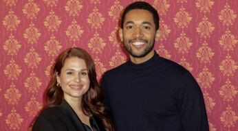 Auf diesem Presse- und Eventfoto zu Ghosts Staffel 2 ARD stehen Cristina do Rego und Benito Bause nebeneinander vor einer rot gemusterten Hintergrundwand. Cristina do Rego trägt ein schwarzes Outfit mit Blazer und lächelt freundlich in die Kamera. Benito Bause trägt einen dunklen Rollkragenpullover und lächelt ebenfalls offen. Die Stimmung wirkt gelöst, professionell und herzlich.