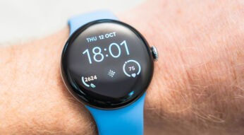Auf dem Bild zur Google Pixel Watch ist eine runde Smartwatch mit schwarzem Display und hellblauem Armband am Handgelenk zu sehen. Die Google Pixel Watch zeigt die Uhrzeit 18:01 sowie Fitnessdaten wie Schritte und Herzfrequenz an. Das minimalistische Design wirkt modern und elegant, während die Nahaufnahme eine klare, ruhige und hochwertige Produktstimmung vermittelt.