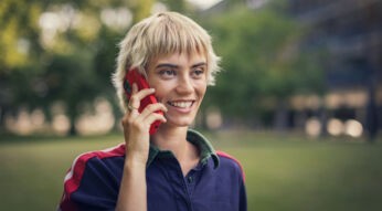 Eher: Lächelnde Frau telefoniert mit ihrem Vodafone Mobil-Tarif im Freien