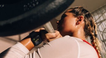 Frau stemmt Langhantel und trägt am linken Handgelenk die Apple Watch Series 12.