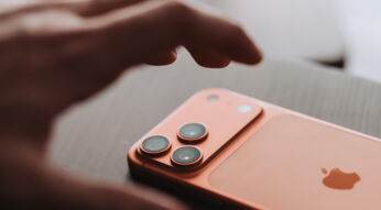 Hand greift nach iPhone 17 Pro Max in Orange, das auf einem Holztisch liegt