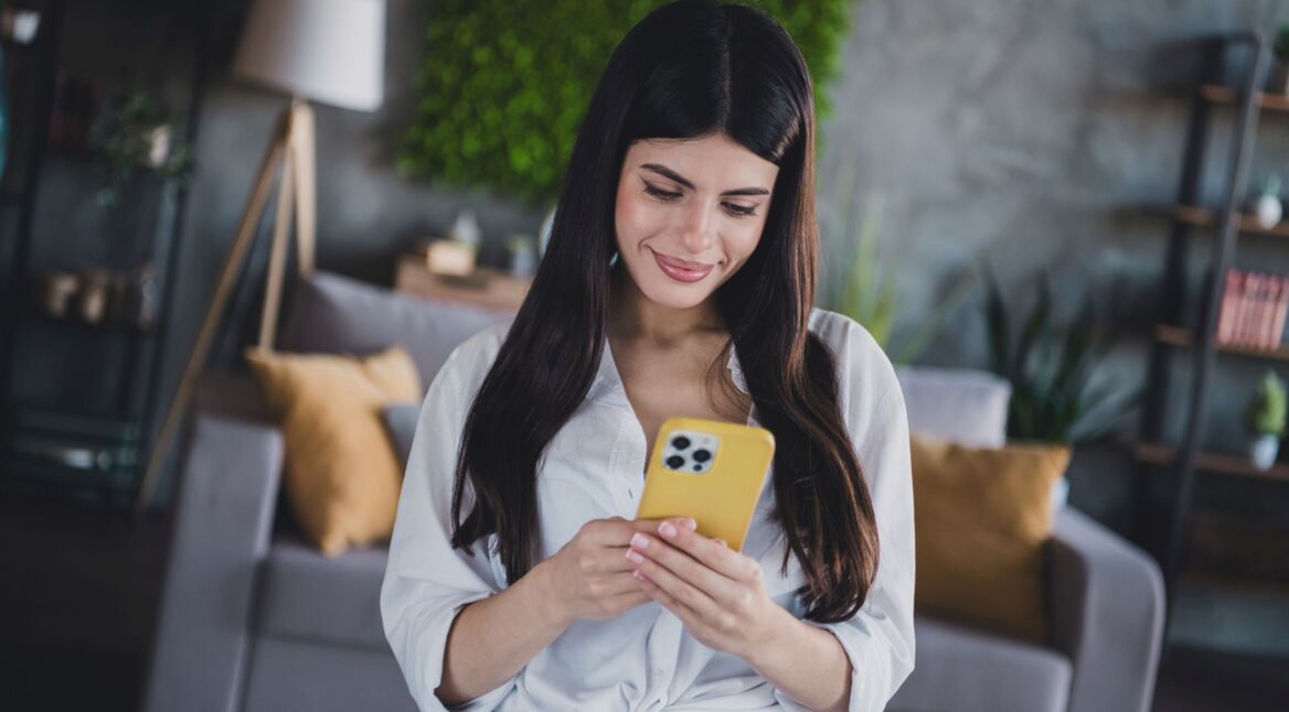 Junge Frau schaut auf ein iPhone mit gelber Hülle.