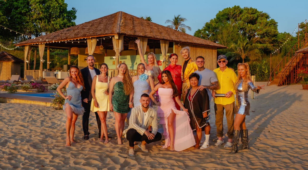 Auf dem Bild zur Show Kampf der RealityAllstars posieren zahlreiche Reality-TV-Persönlichkeiten barfuß am Sandstrand vor einer tropischen Villa. Zu sehen sind u.a. Georgina Fleur, Sandy Fähse, Yeliz Koc, Tayisiya und Yana Morderger, Serkan Yavuz, Kader Loth, Giuliana Farfalla, Kate Merlan, Sam Dylan, Narumol, Paco Herb, Prinz Frédéric von Anhalt und Loona. Die Stimmung wirkt ausgelassen und sommerlich.