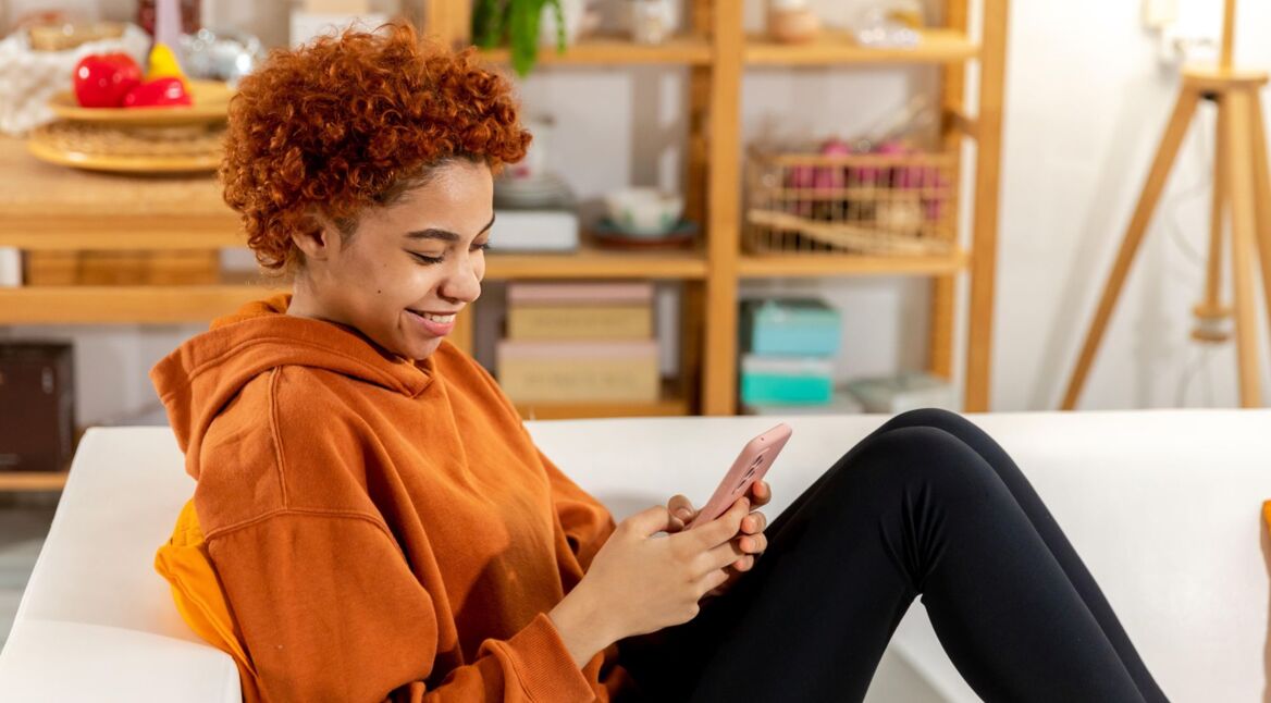 Eine junge Frau sitzt auf dem Sofa und surft auf dem Handy im Internet.