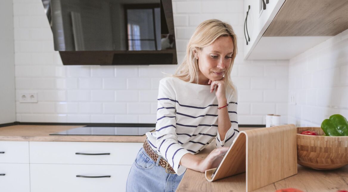 Eine junge Frau arbeitet in der Küche auf ihrem Tablet-PC.