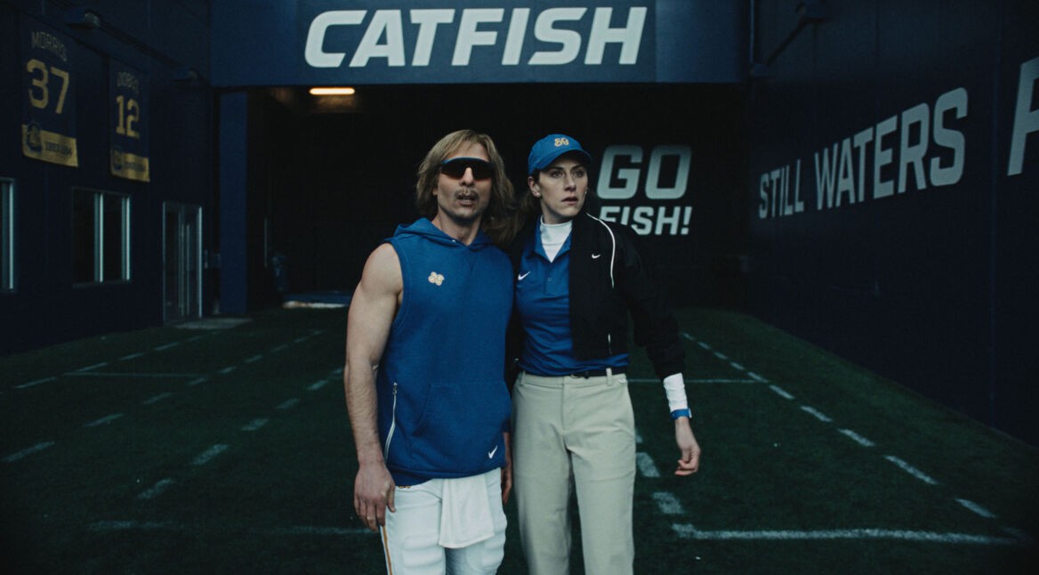 Glen Powell als Chad Powers mit blonder Perücke und Sonnenbrille steht mit Trainerin im „Catfish“-Tunnel Staffel 2 auf Disney+.