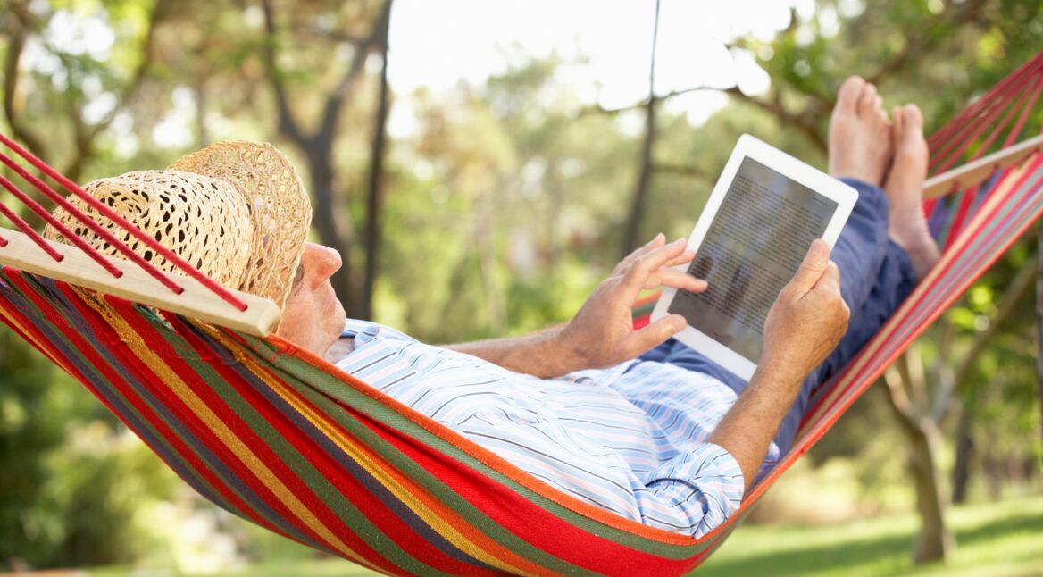 Senior Man Relaxing In Hammock With  E-Book