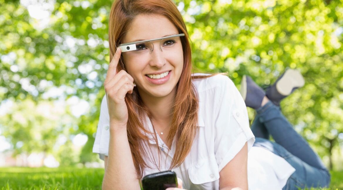 Woman at the park smiling and using google glass and a mobile phone