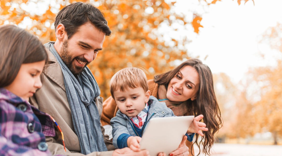 Smiling parents teaching their children how to use touchpad outdoors.