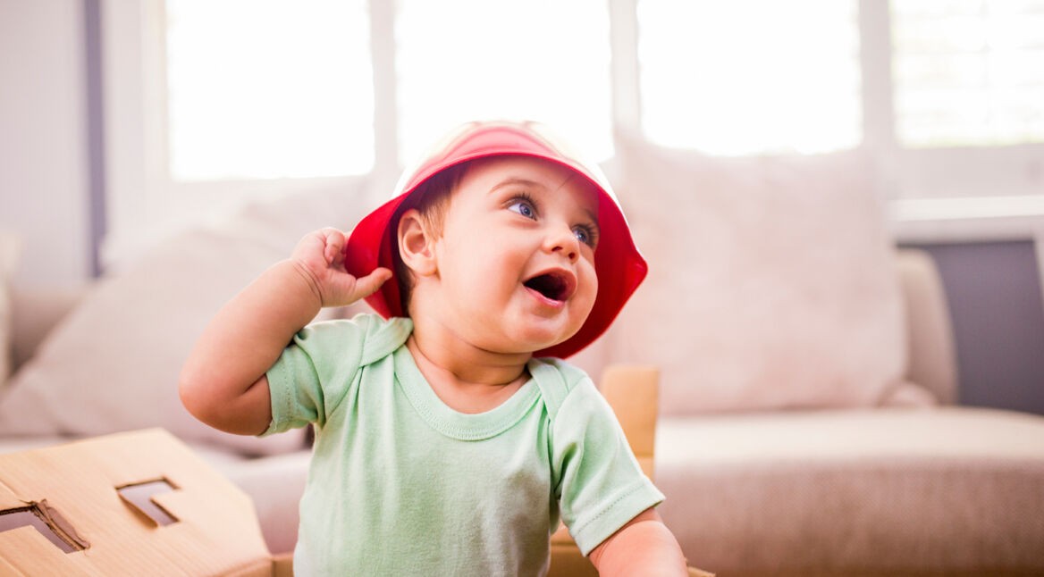 Excited baby wearing a plastic bowl as a hat