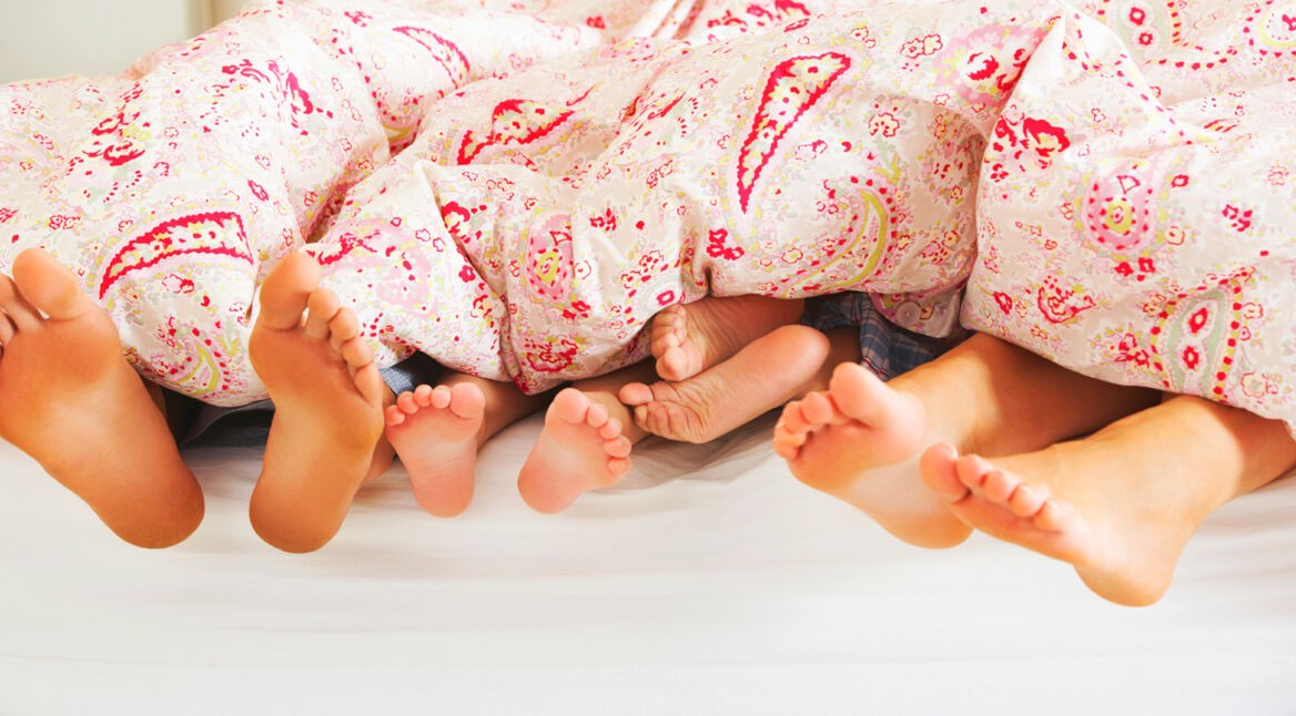 Family's Feet Poking Out From Duvet In Bed