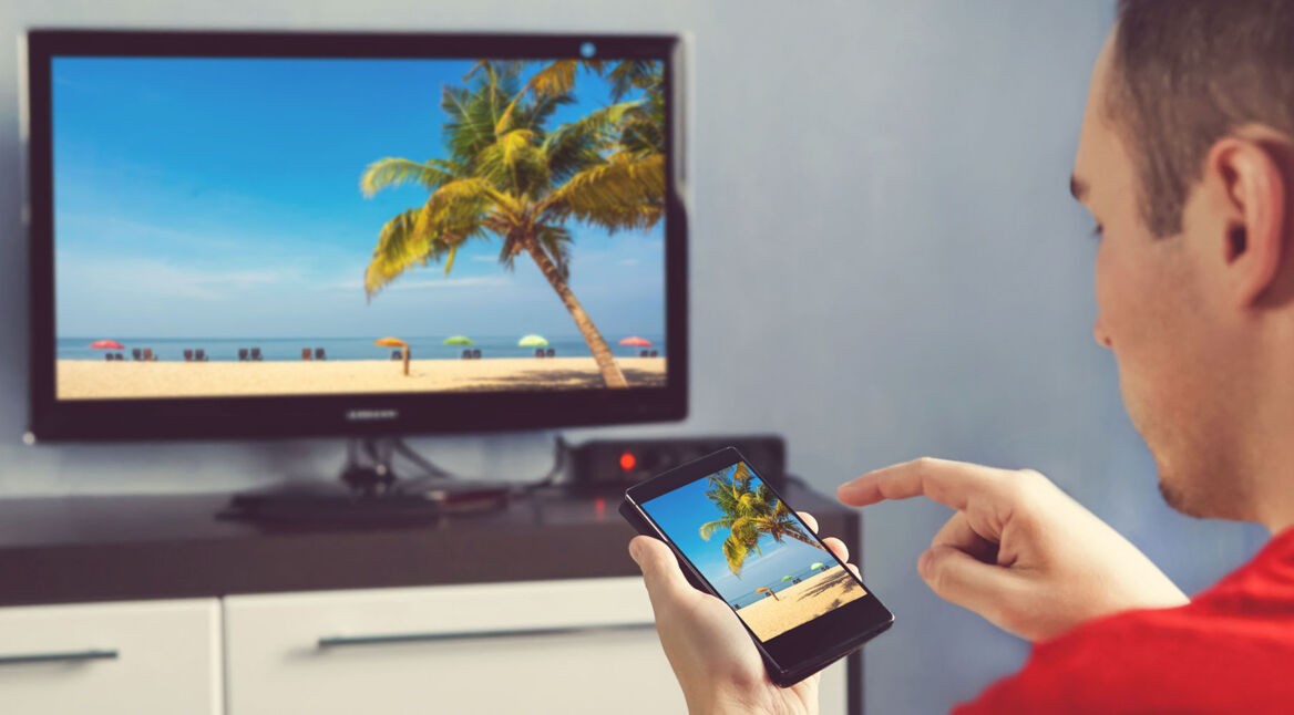 Mann sieht sich Urlaubsfotos vom Handy auf dem TV an