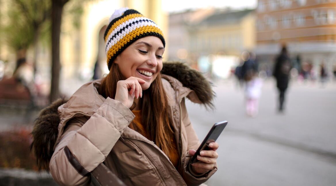 Frau sitzt mit Smartphone in der Hand auf einer Bank.