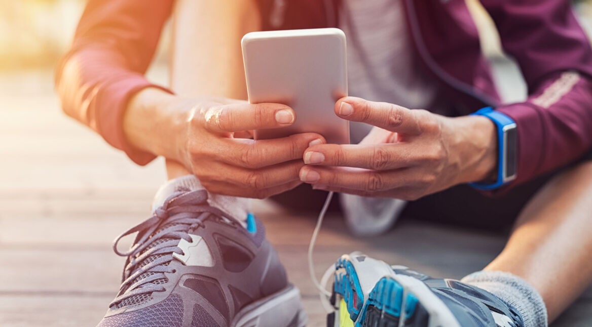 Mann mit Sportschuhen sitzt auf dem Boden und hält Smartphone in der Hand