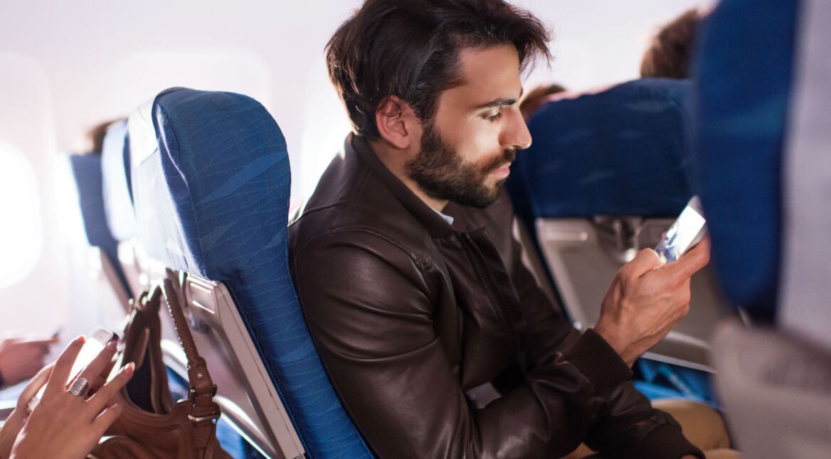 Mann sitzt im Flugzeug und spielt auf dem Smartphone.