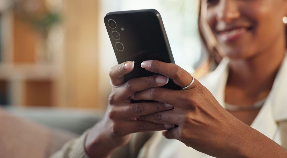 Junge Frau schaut lächelnd auf ihr Android-Handy.