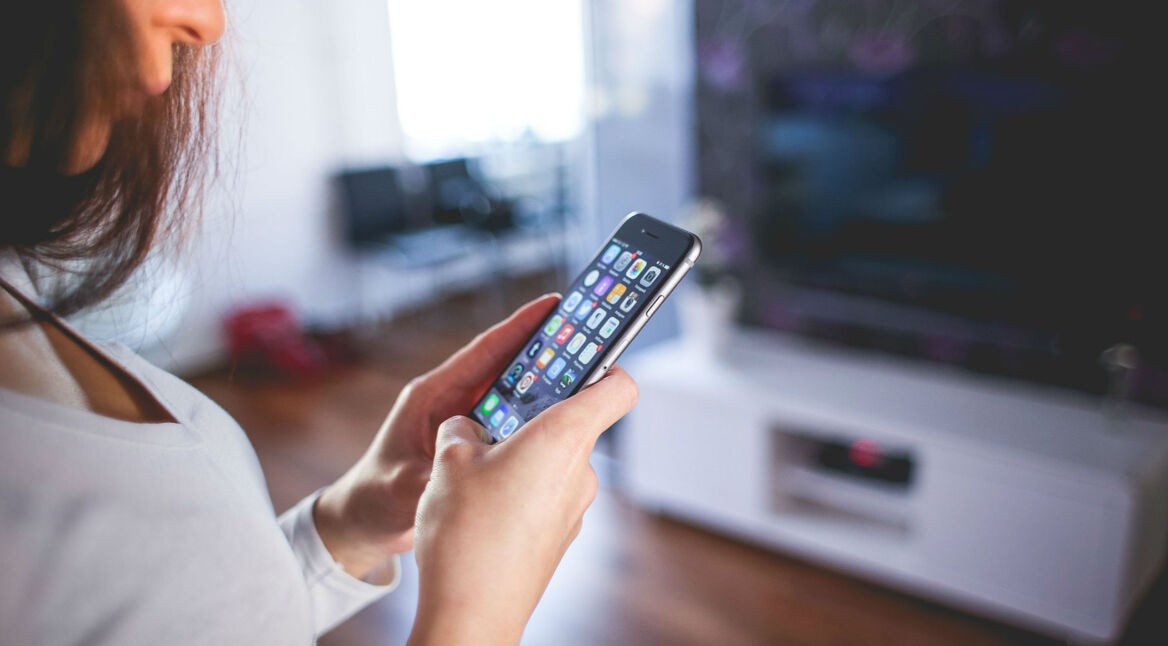 Frau hält im Wohnzimmer ein iPhone in der Hand.