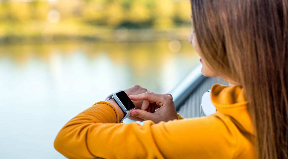 Frau in gelber Jacke schaut auf ihre Smartwatch.