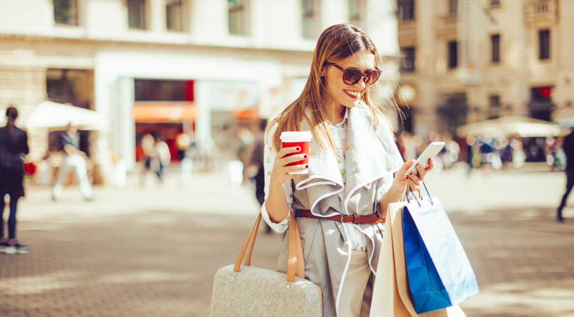 Frau mit Handy und Kaffeebecher beim Shopping