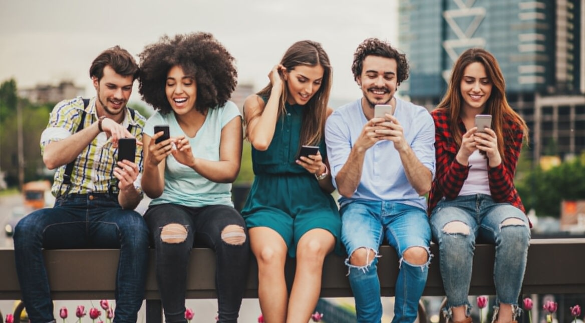 Gruppe junger Leute auf einem Balken mit Handies