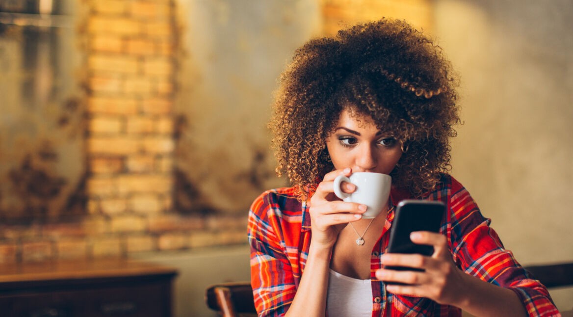 Frau mit Afro-Frisur trinkt Kaffee am Handy