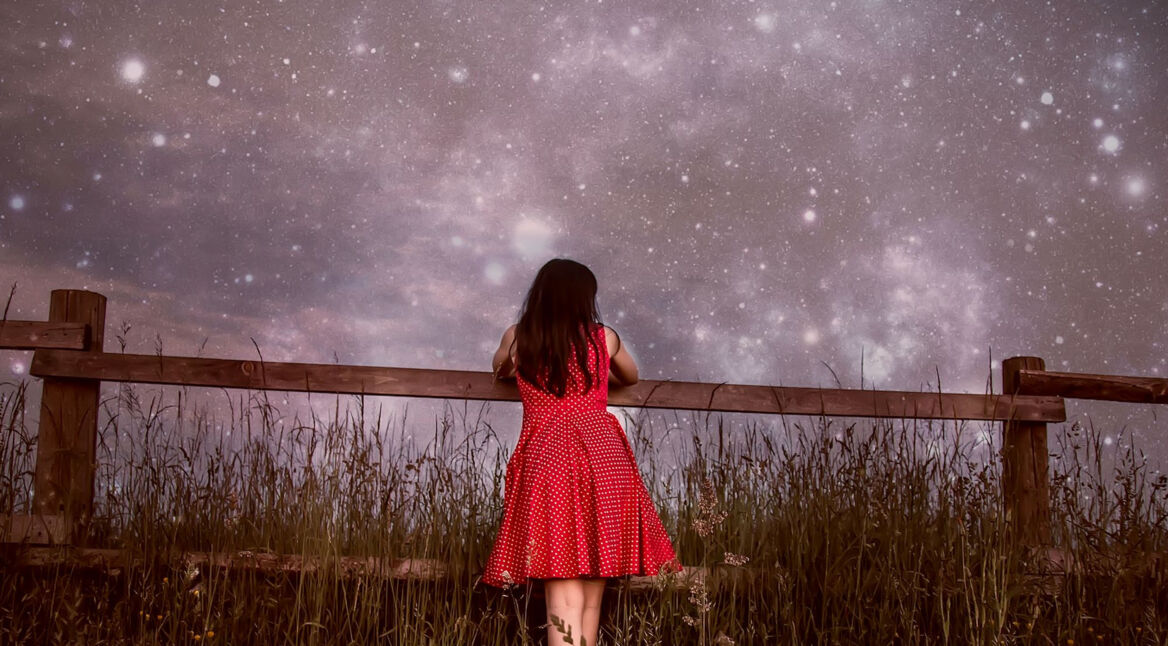 Mädchen lehnt an Zaun vor Sternenhimmel