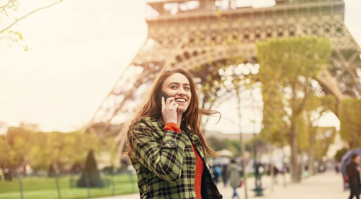 Frau telefoniert am Eiffelturm mit dem Smartphone.