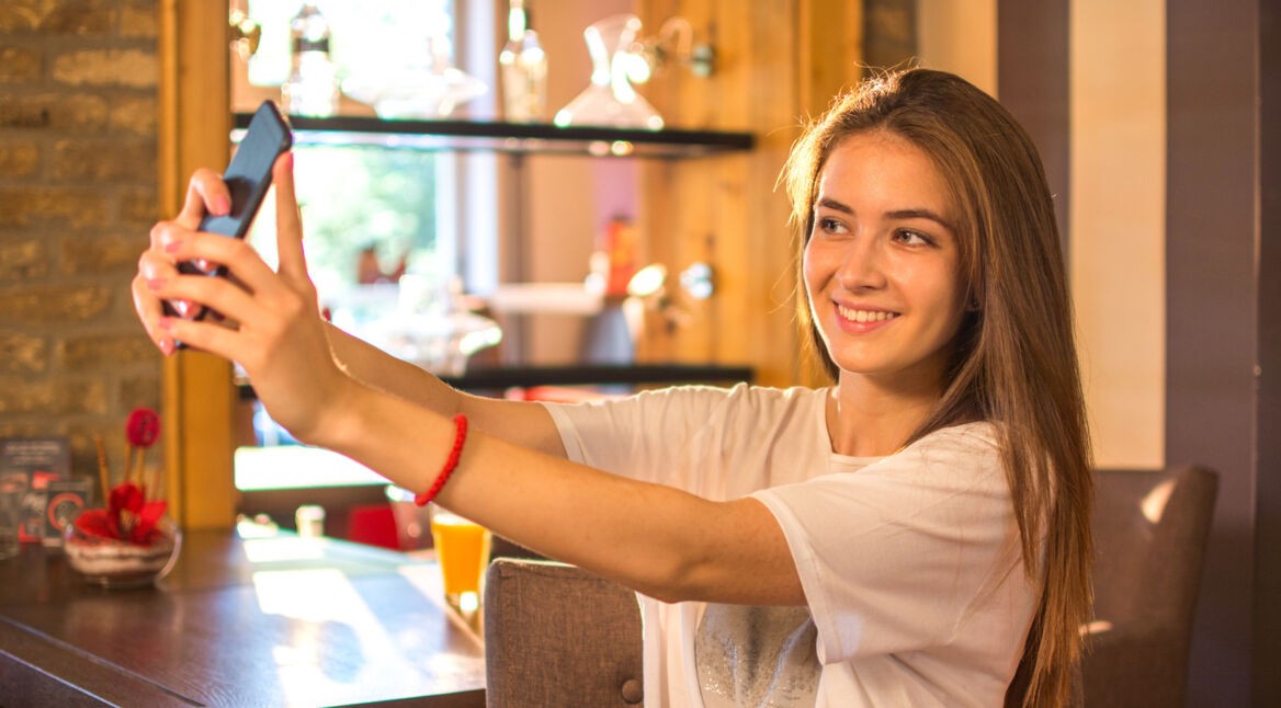 Frau macht im Cafe ein Selfie mit ihrem Smartphone