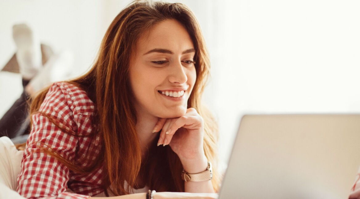 Frau in rotkariertem Hemd im Bett vor dem Laptop