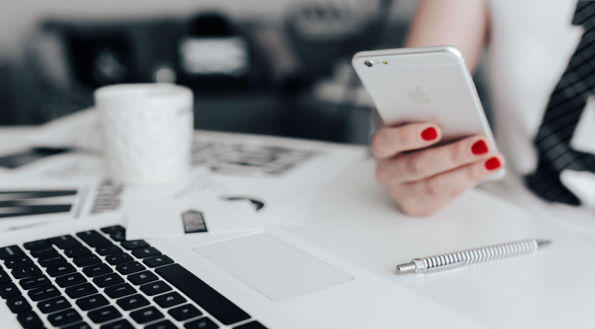 Frau mit rotlackierten Nägeln und iPhone in der Hand.