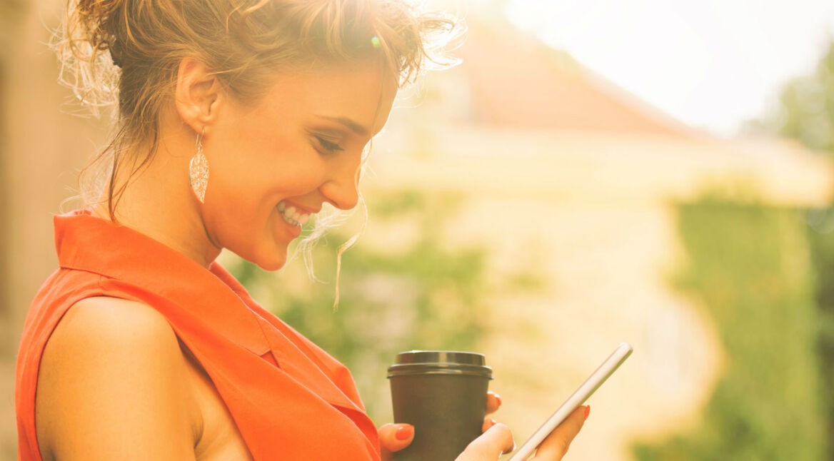 Frau mit Kaffeebecher und Smartphone in der Hand.