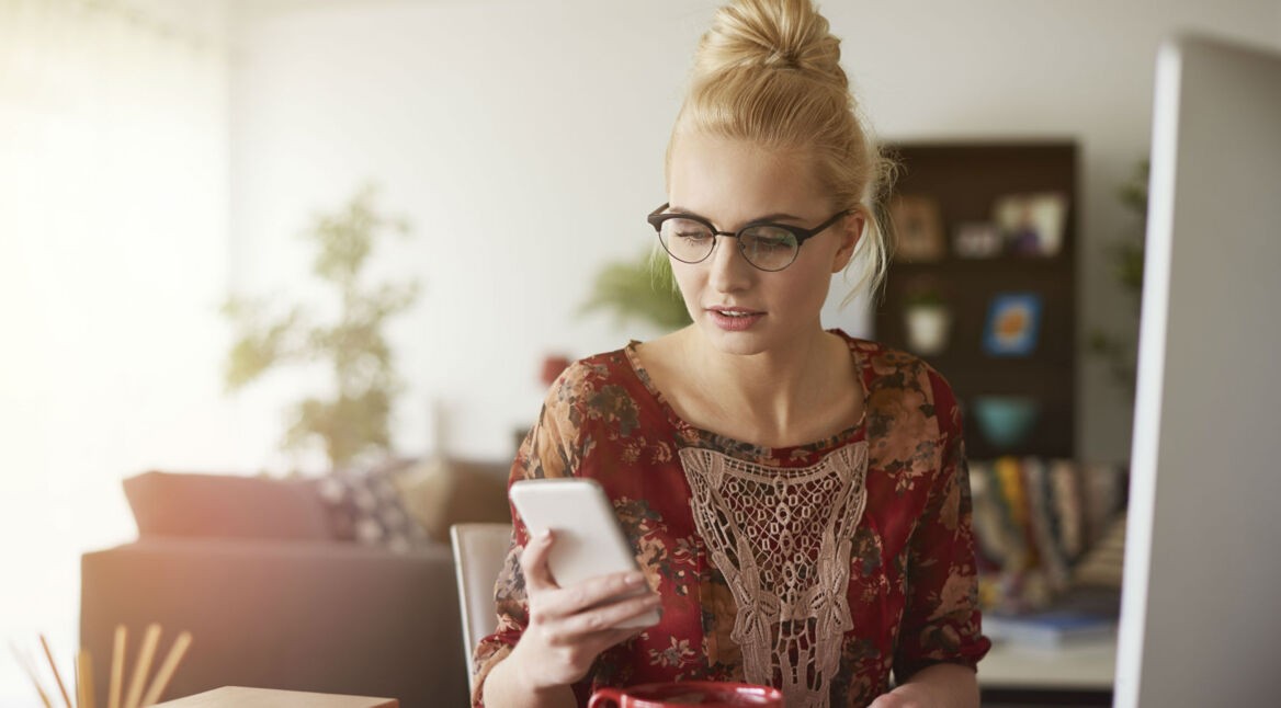 Frau mit blonden Haaren und Brille schaut ihr Smartphone.