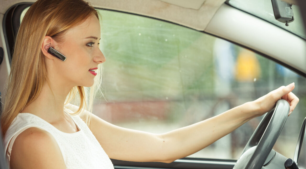 Frau nutzt Bluetooth-Headset beim Autofahren