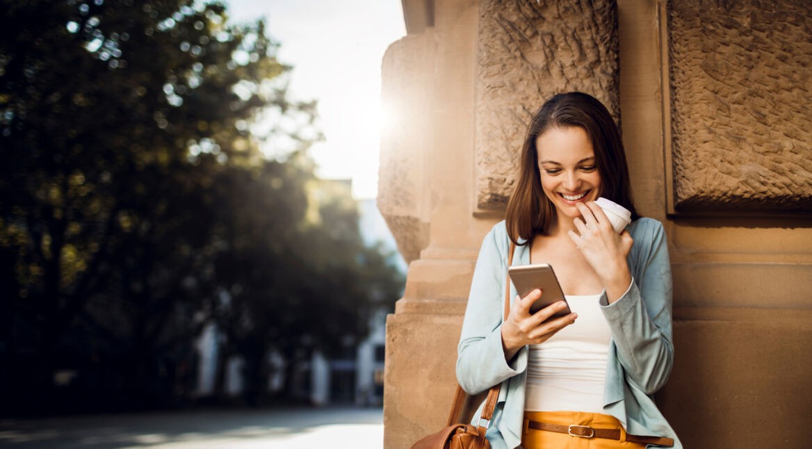 Frau steht vor einer Wand mit Smartphone im Sonnenuntergang