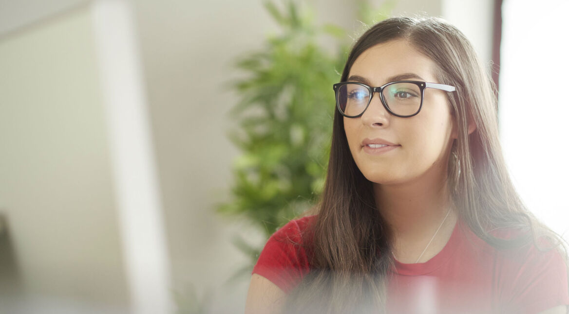 Mädchen mit Brille und rotem T-Shirt sitzt vor einem Computer.