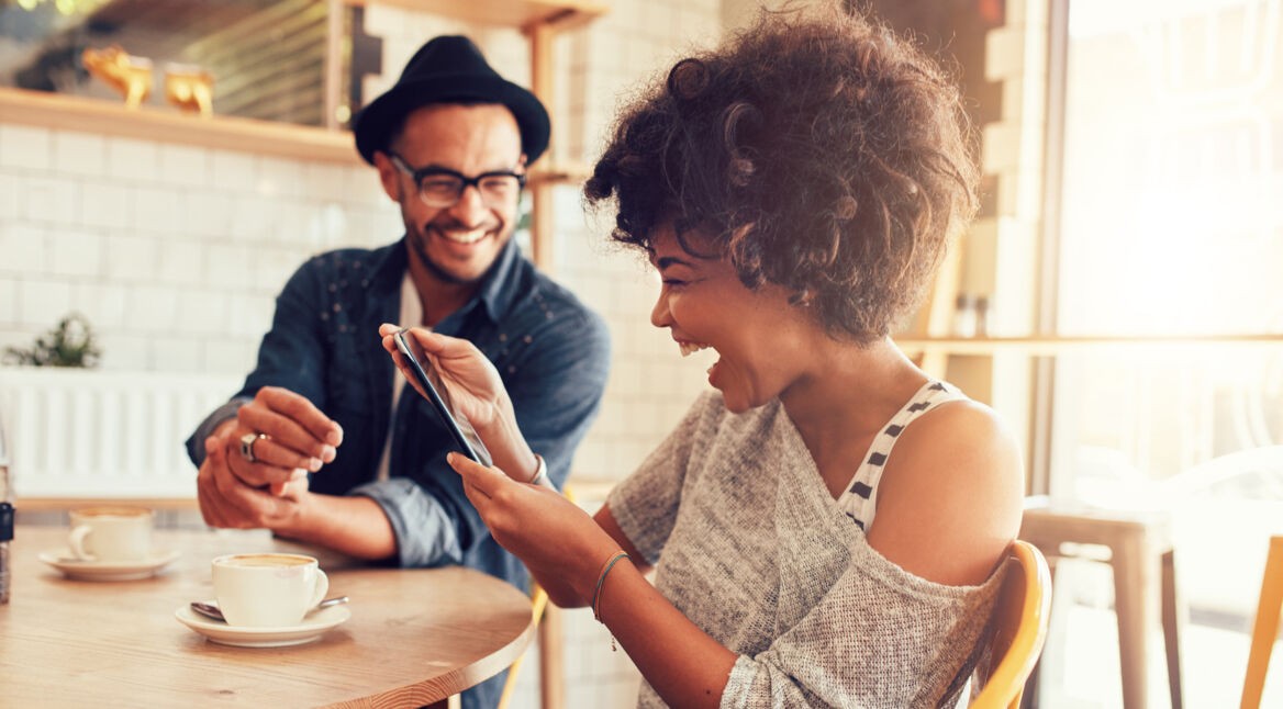 Mann und Frau im Cafe lachen über Witze auf dem Smartphone
