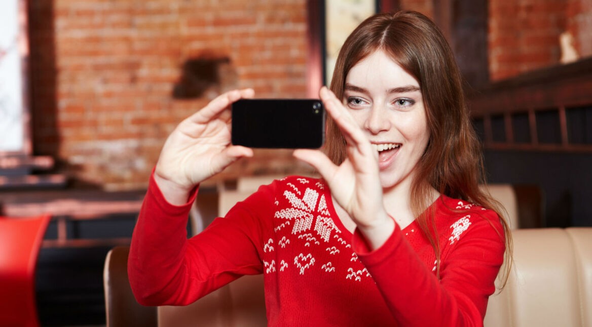 Frau im roten Pulli nimmt Video mit ihrem Smartphone auf.