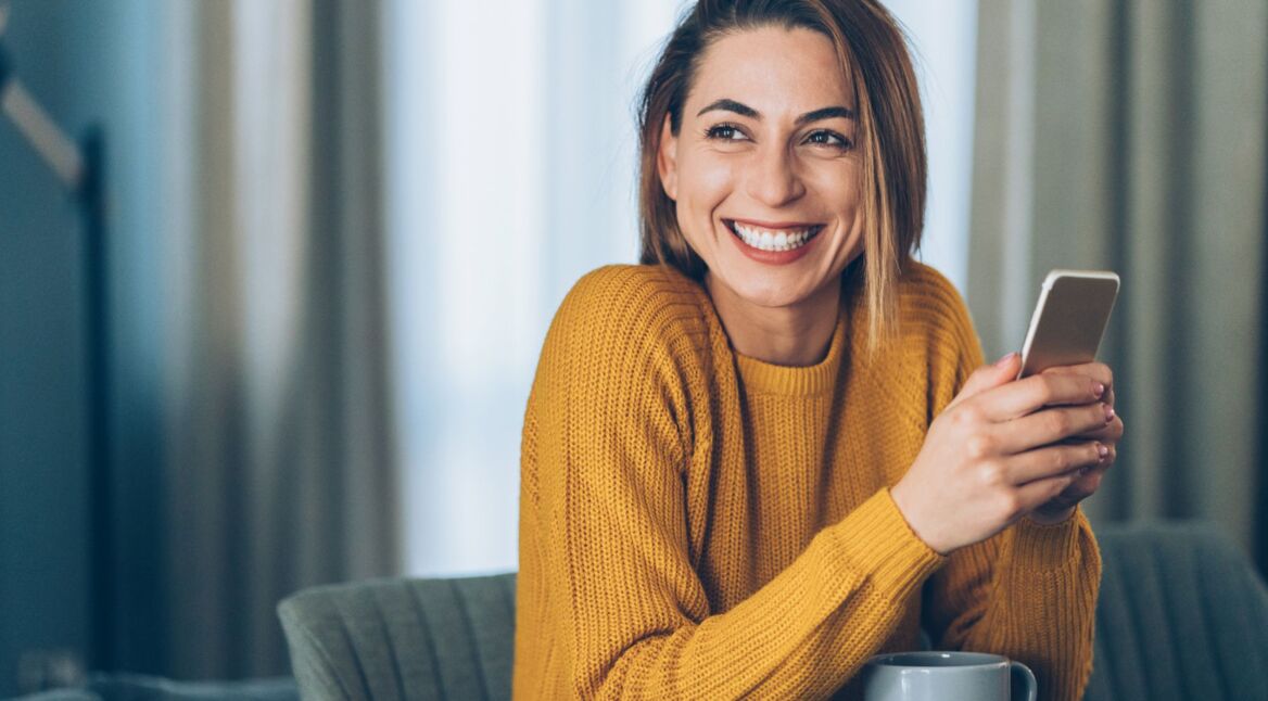 Frau lächelt und hält ein Smartphone in der Hand.