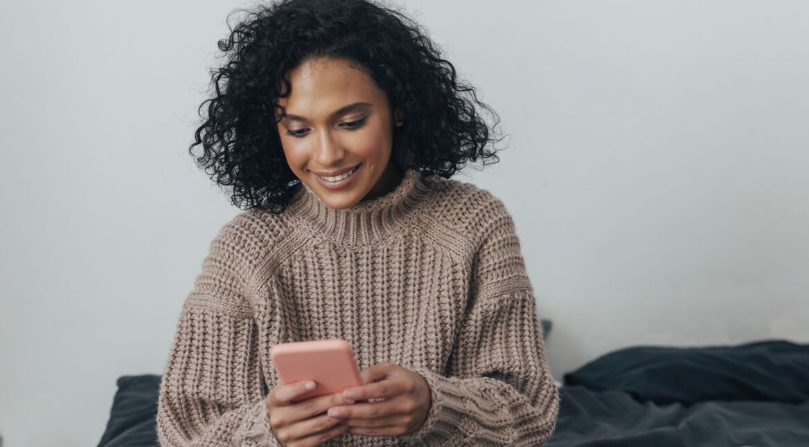 Frau schaut lächelnd auf ihr Handy.
