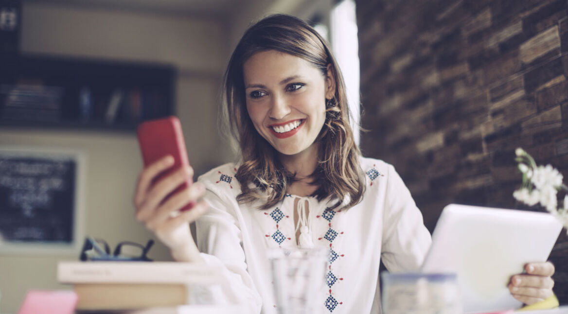 Frau im Büro schaut auf ihr rotes Smartphone.