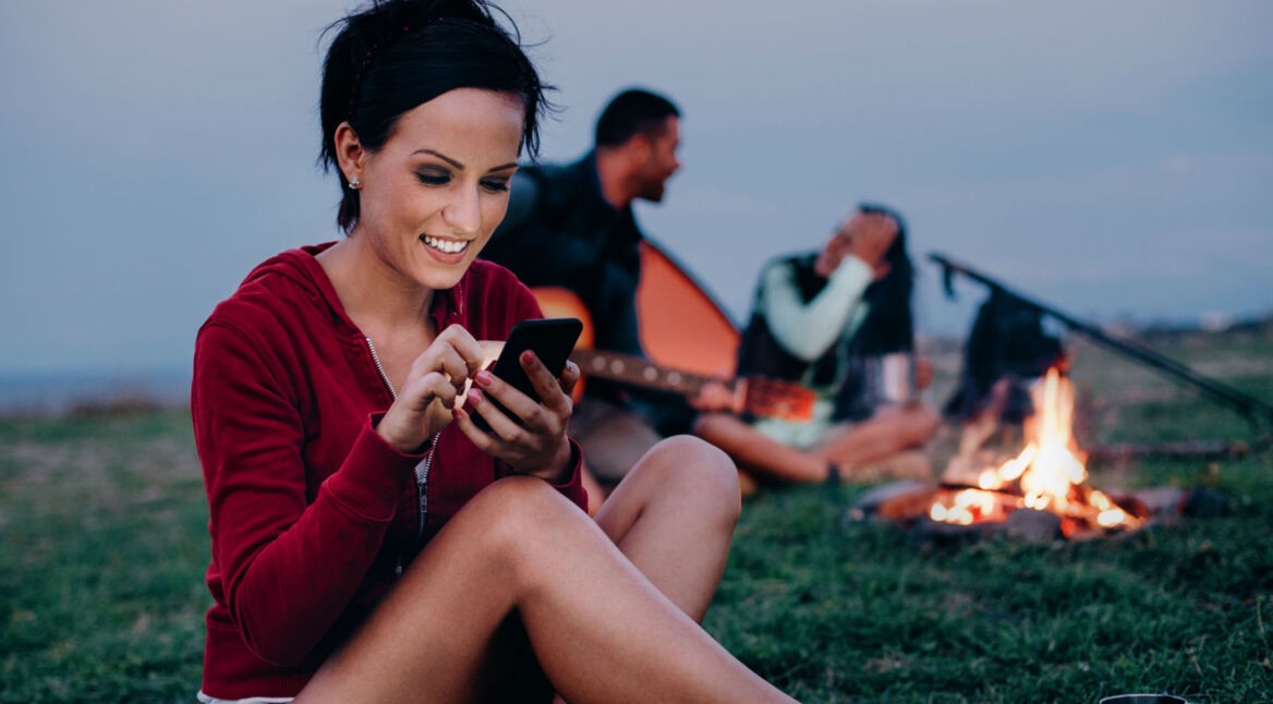 Frau mit Smartphone und eine Feuerstelle im Hintergrund.