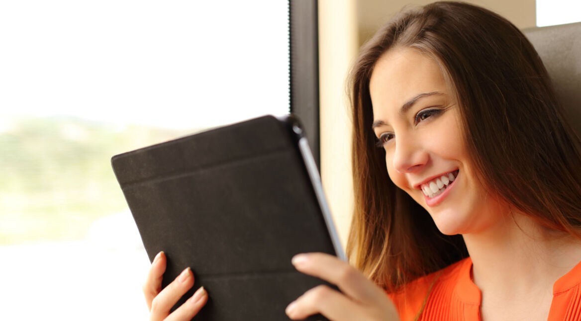 Frau sitzt im Zug und liest etwas auf ihrem Tablet.