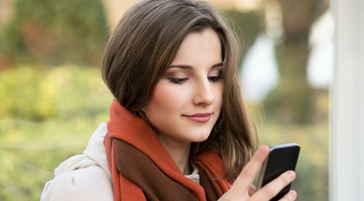 Junge Frau mit orangem Schal schaut auf ihr Smartphone.