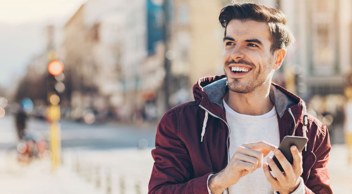 Junger Mann lächelt, während er ein Smartphone in der Hand hält.