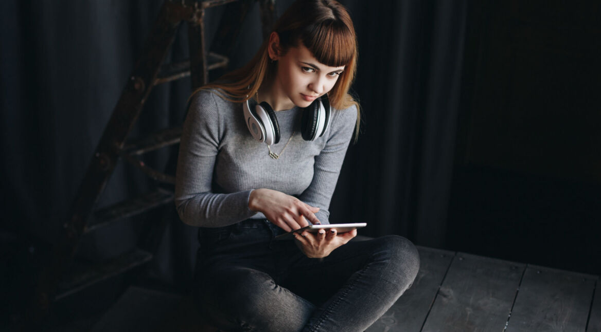 Junges Mädchen sitzt mit Tablet in der Hand auf Holz.